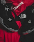 Black athletic shoes are placed alongside red and black sportswear bearing logos from Spalding and The North Face.