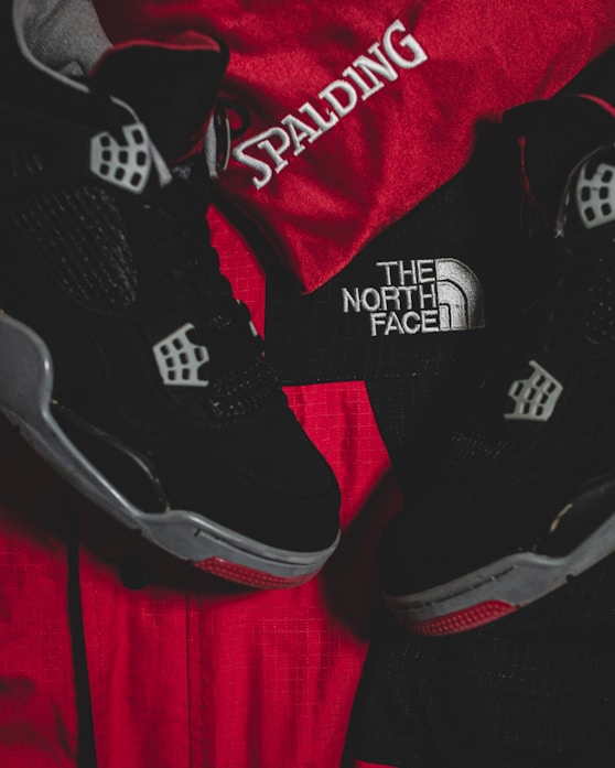 Black athletic shoes are placed alongside red and black sportswear bearing logos from Spalding and The North Face.