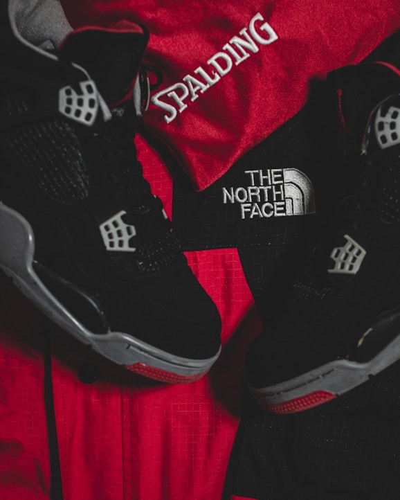 Black athletic shoes are placed alongside red and black sportswear bearing logos from Spalding and The North Face.