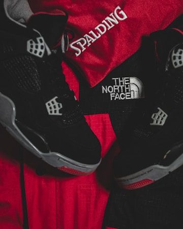 Black athletic shoes are placed alongside red and black sportswear bearing logos from Spalding and The North Face.