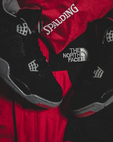 Black athletic shoes are placed alongside red and black sportswear bearing logos from Spalding and The North Face.