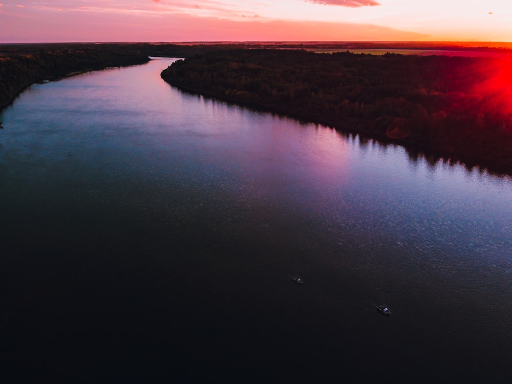 body of water near brown field during sunset