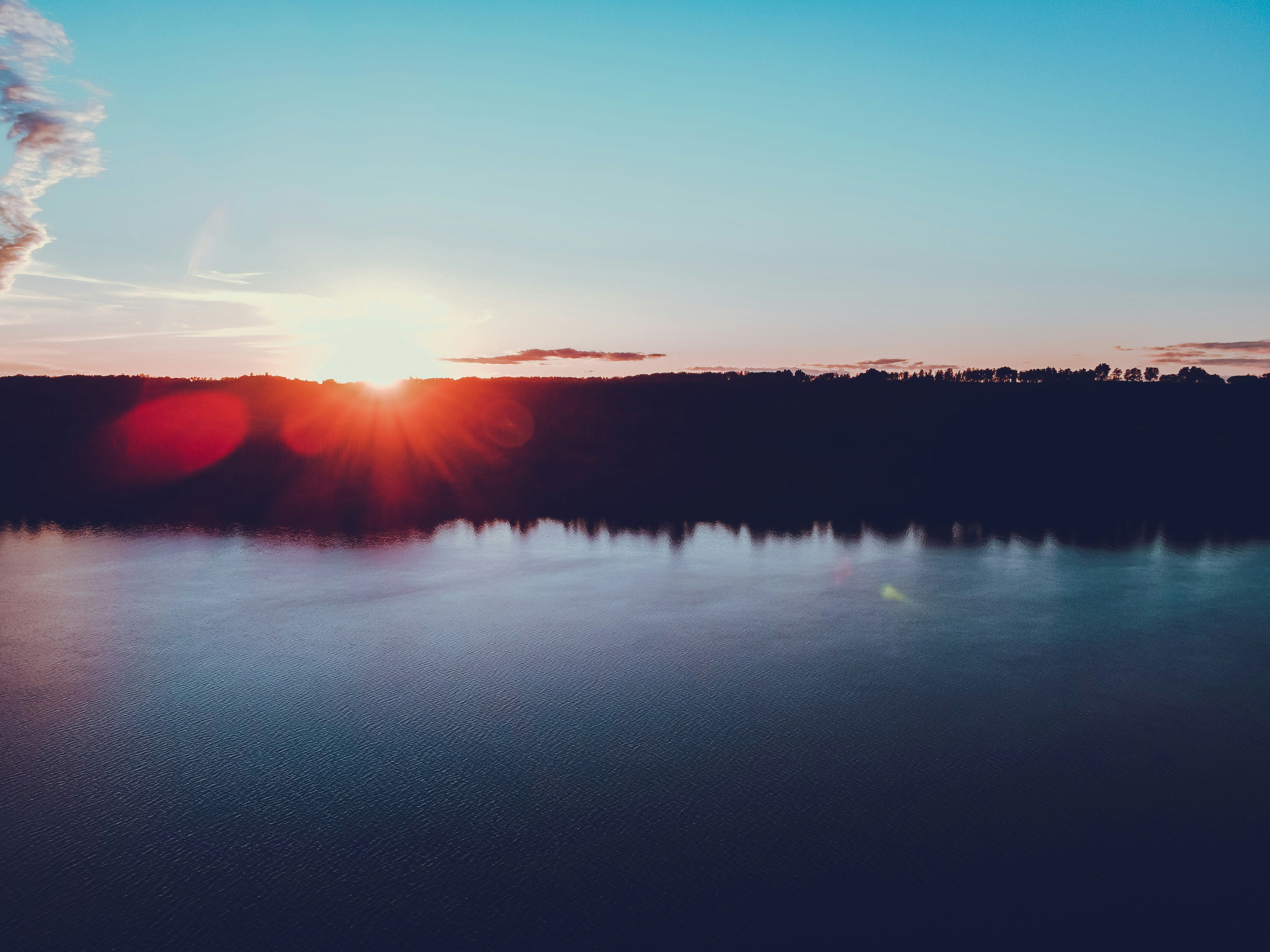 body of water near trees during sunset