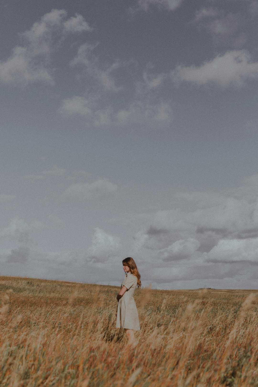 woman in white dress standing on brown grass field under white clouds during daytime