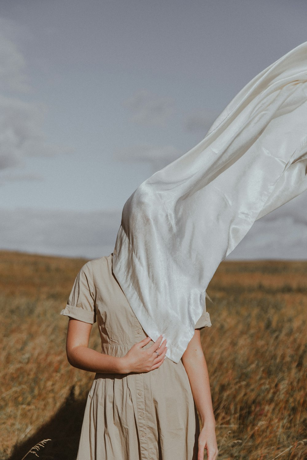 mulher na camisa branca de manga comprida e saia branca em pé no campo de grama marrom durante o dia
