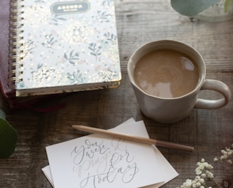 white and purple floral notebook beside white ceramic mug