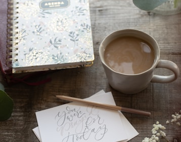 white and purple floral notebook beside white ceramic mug