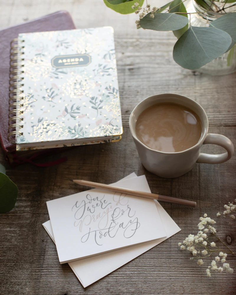 Geöffnetes Notizbuch mit floralem Muster neben einer weißen Keramiktasse auf einem Schreibtisch
