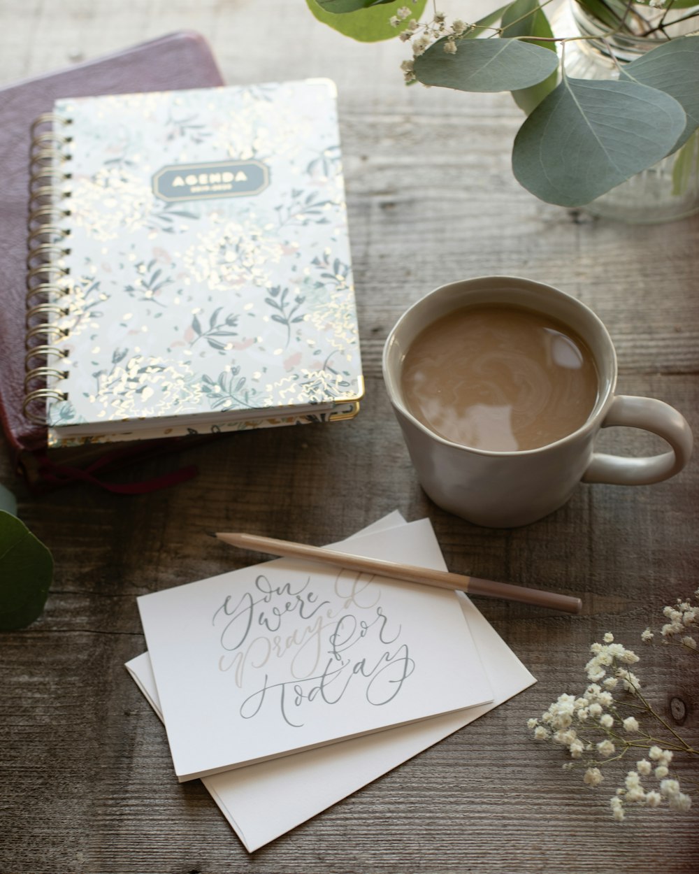 white and purple floral notebook beside white ceramic mug