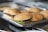 Several hamburgers arranged on a metal tray, each containing a patty with lettuce inside soft buns. The surface below the tray appears to be part of a kitchen setting.