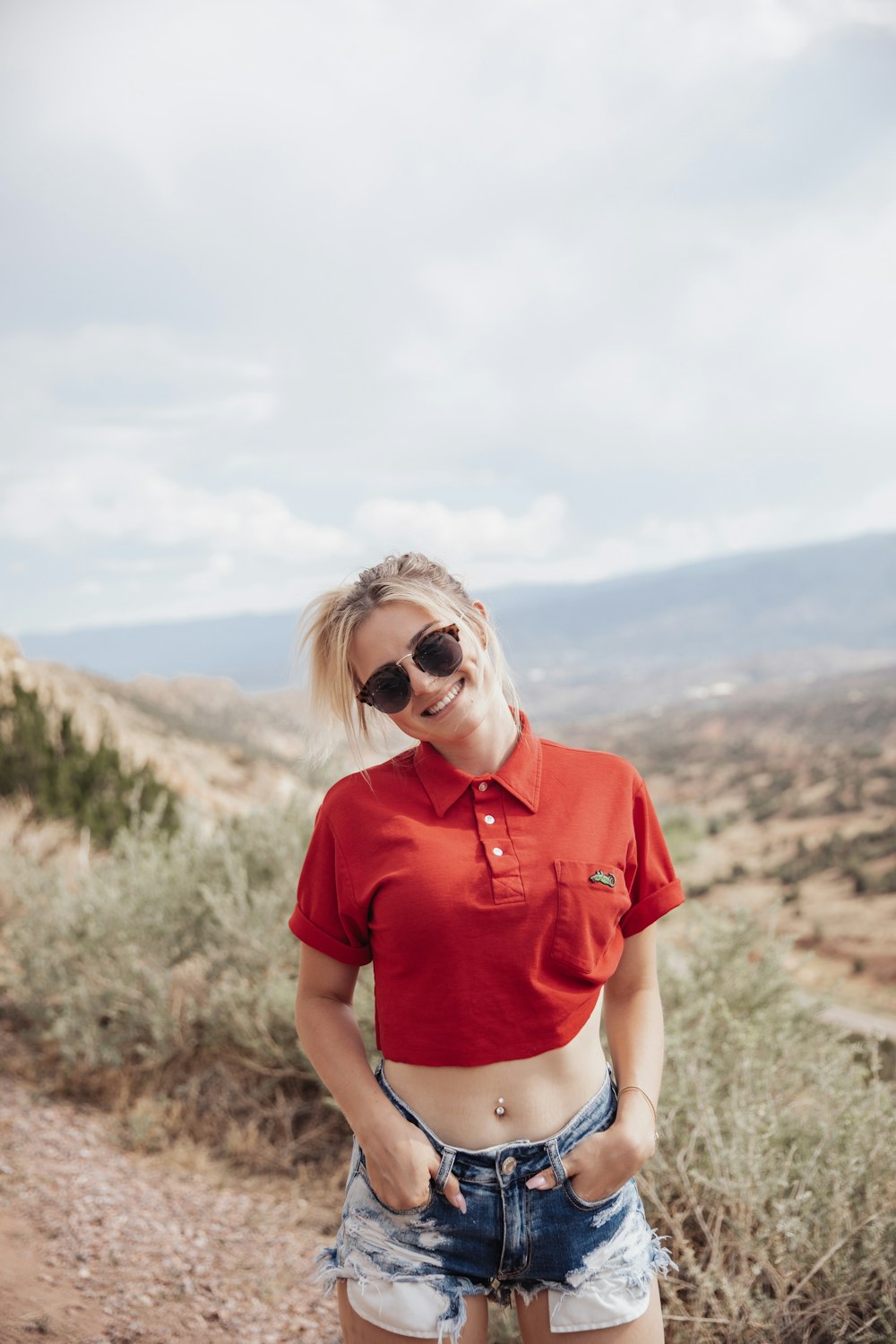 赤いクルーネックのTシャツとブルーデニムのデイジーデュークスが茶色の野原に立つ女性