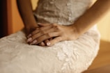 Hands gently adjusting the satin fabric of a high-neck bridal gown on a mannequin.