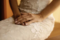 Close-up of a woman’s delicate hands resting on silk sheets in soft focus.