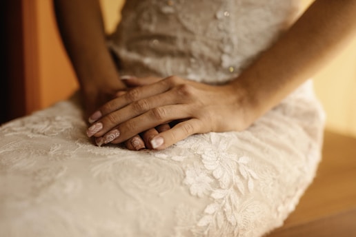 A close-up of perfectly manicured hands resting gently on a soft white towel, with subtle pink accents in the background.