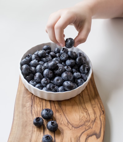 person holding bowl of black berries
