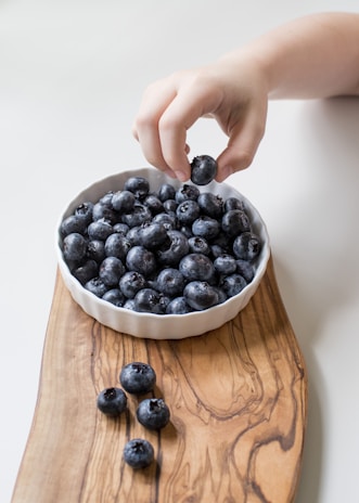 person holding bowl of black berries