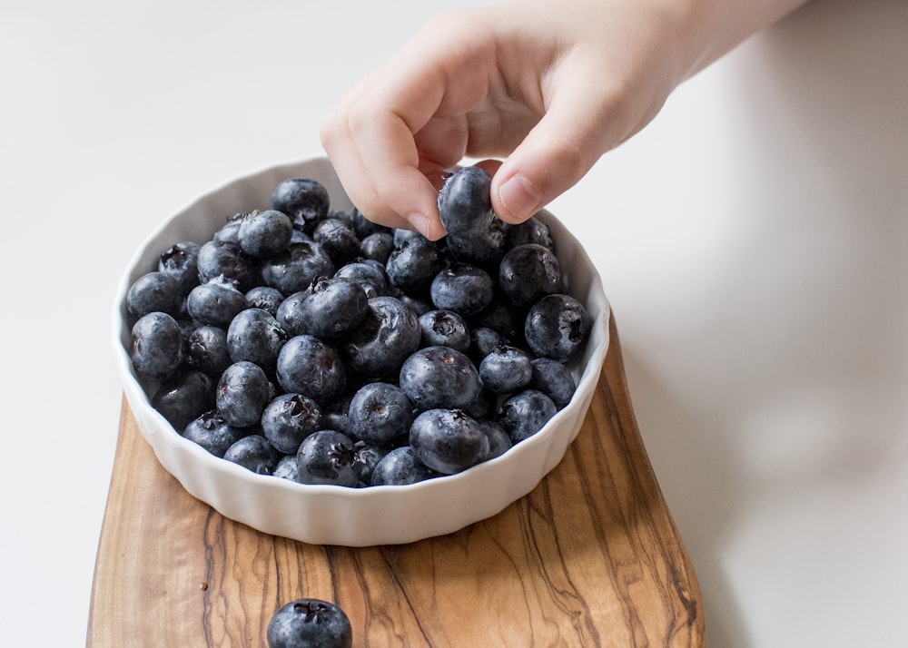 person holding bowl of black berries