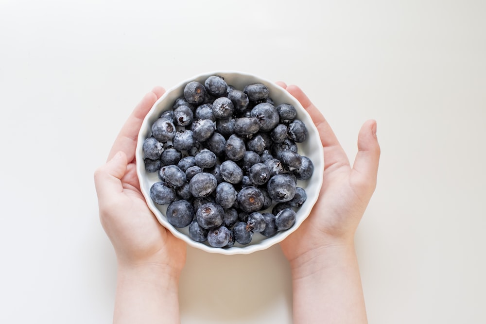 person holding white ceramic bowl with black berries