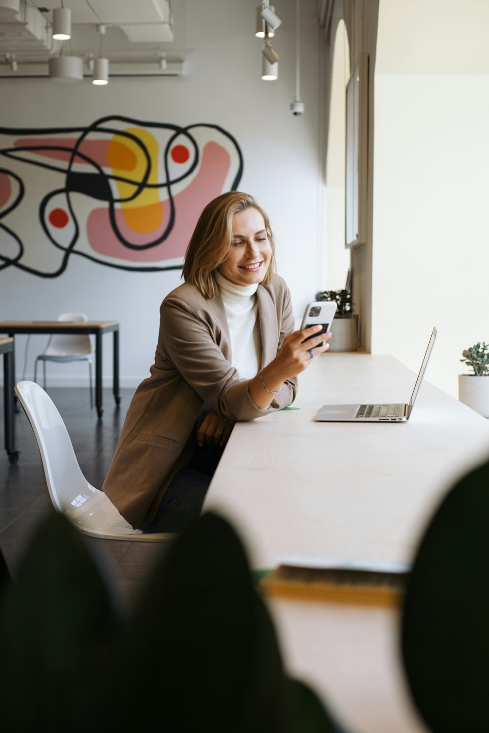 woman in brown blazer sitting on chair holding smartphone