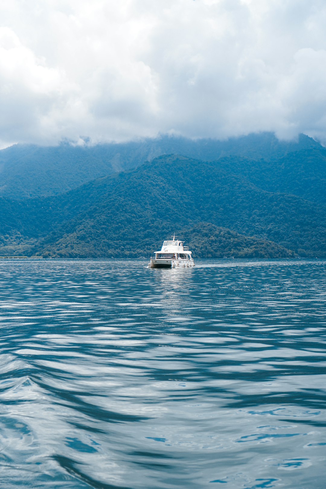 white boat on sea near green mountain under white clouds during daytime