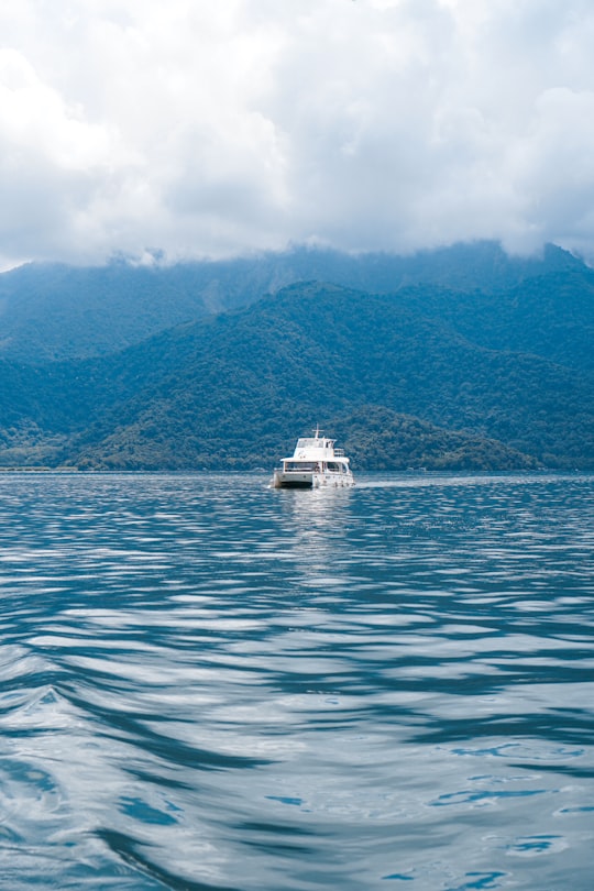 white boat on sea near green mountain under white clouds during daytime in Sun Moon Lake Taiwan