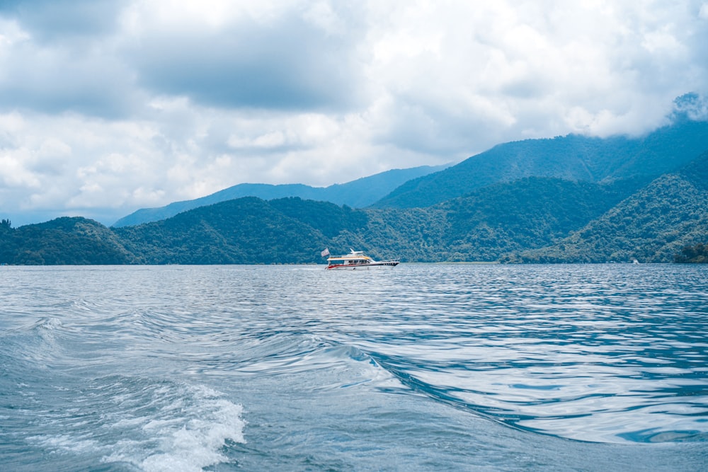 white boat on sea near mountain under white clouds during daytime