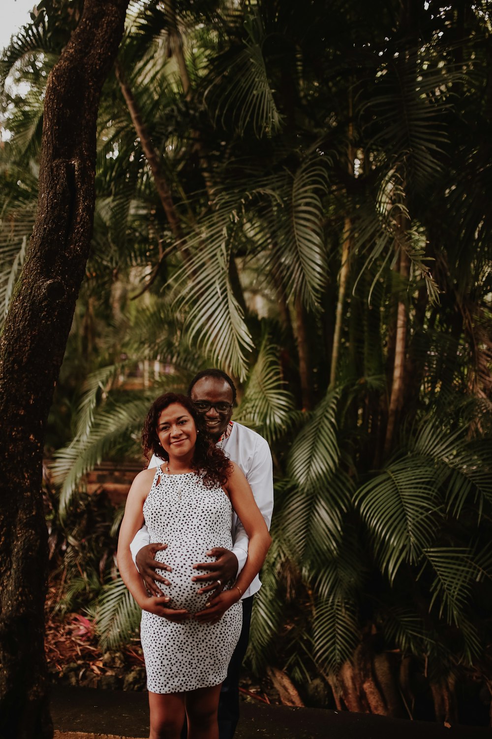 woman in white and black floral dress standing near green palm tree during daytime