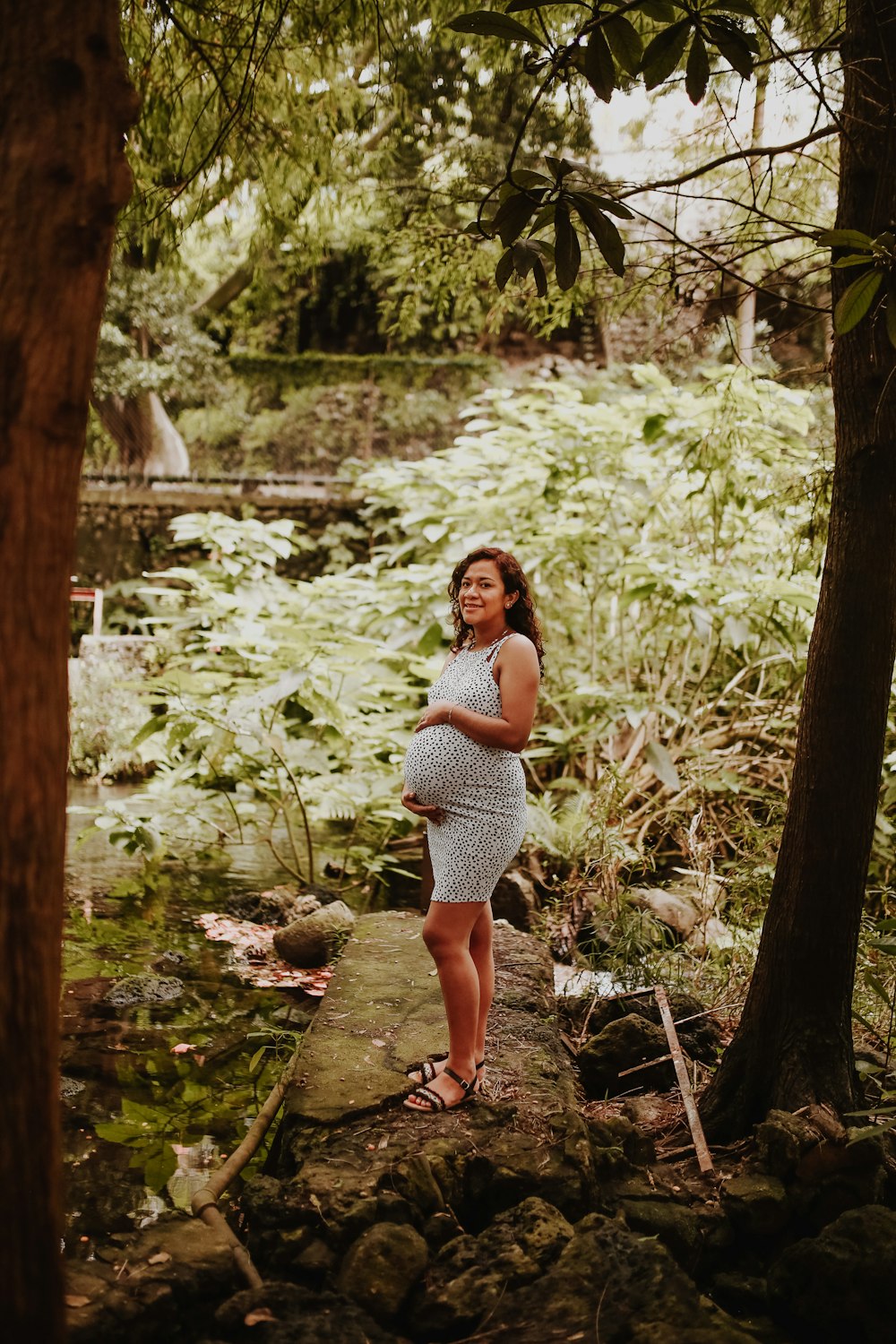 woman in white and black polka dot dress standing on brown tree trunk during daytime