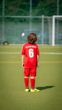 a young boy in a red uniform standing on a soccer field