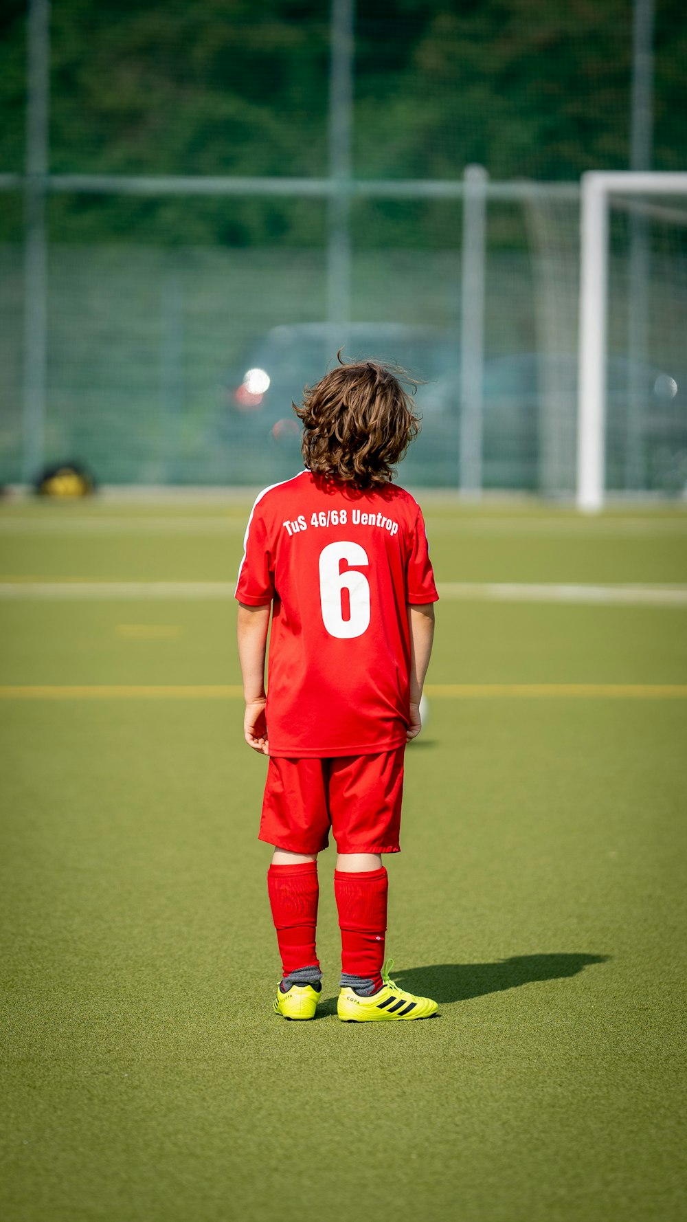 a young boy in a red uniform standing on a soccer field