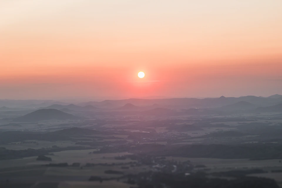 Breathtaking sunset over a vast, flat landscape with rolling hills and scattered trees