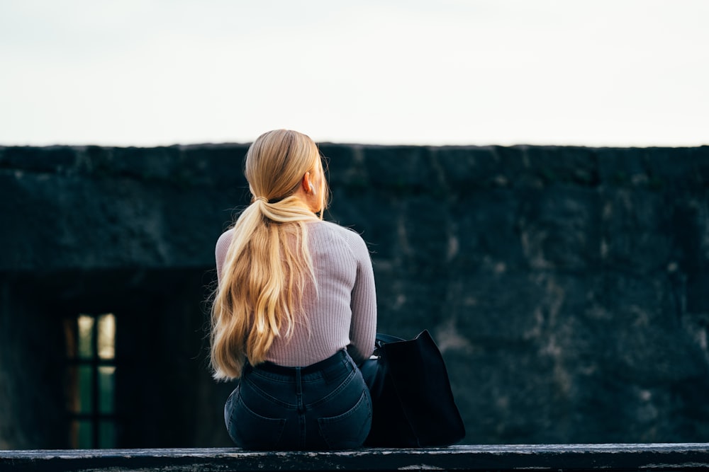 woman in white long sleeve shirt and black denim jeans sitting on gray concrete wall during