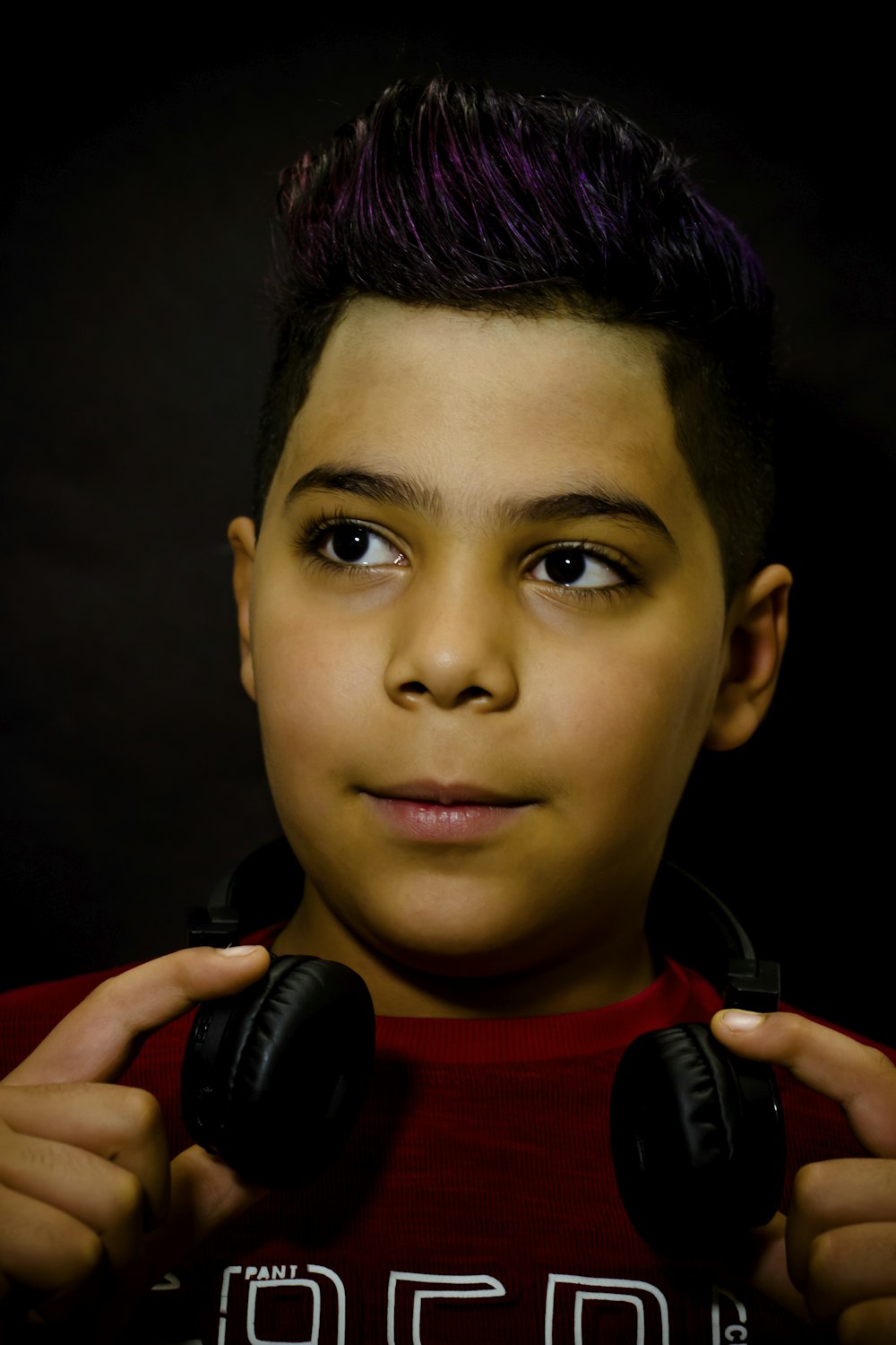 boy in red crew neck shirt holding black wireless headphones