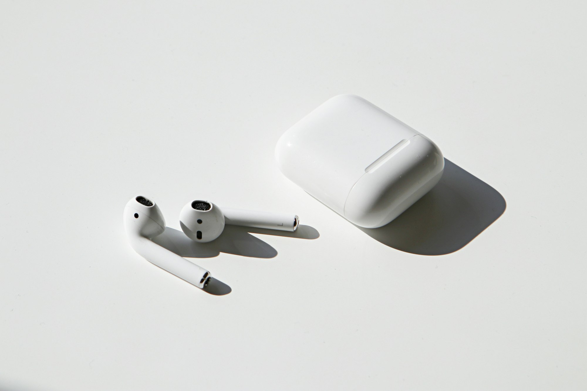 Photo of Apple AirPods on white table with case beside them.