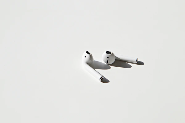 A sleek wireless earbud set resting on a minimalist white surface with soft natural light highlighting its compact design.