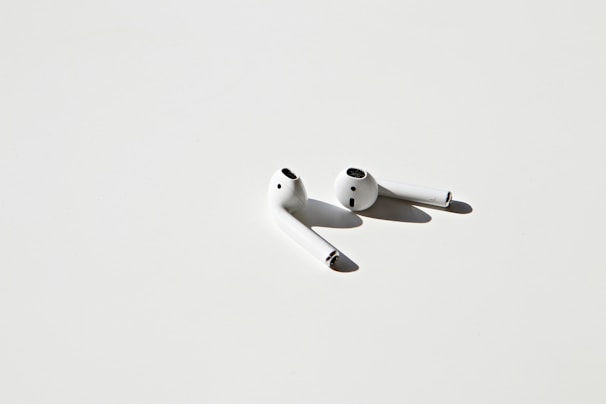 A stylish pair of wireless earbuds resting on a minimalist white surface with soft shadows.