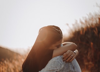 woman in black long sleeve shirt and blue denim jeans covering her face with her hand