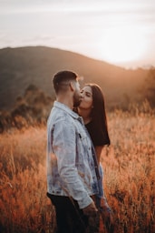 man and woman kissing on brown grass field during daytime