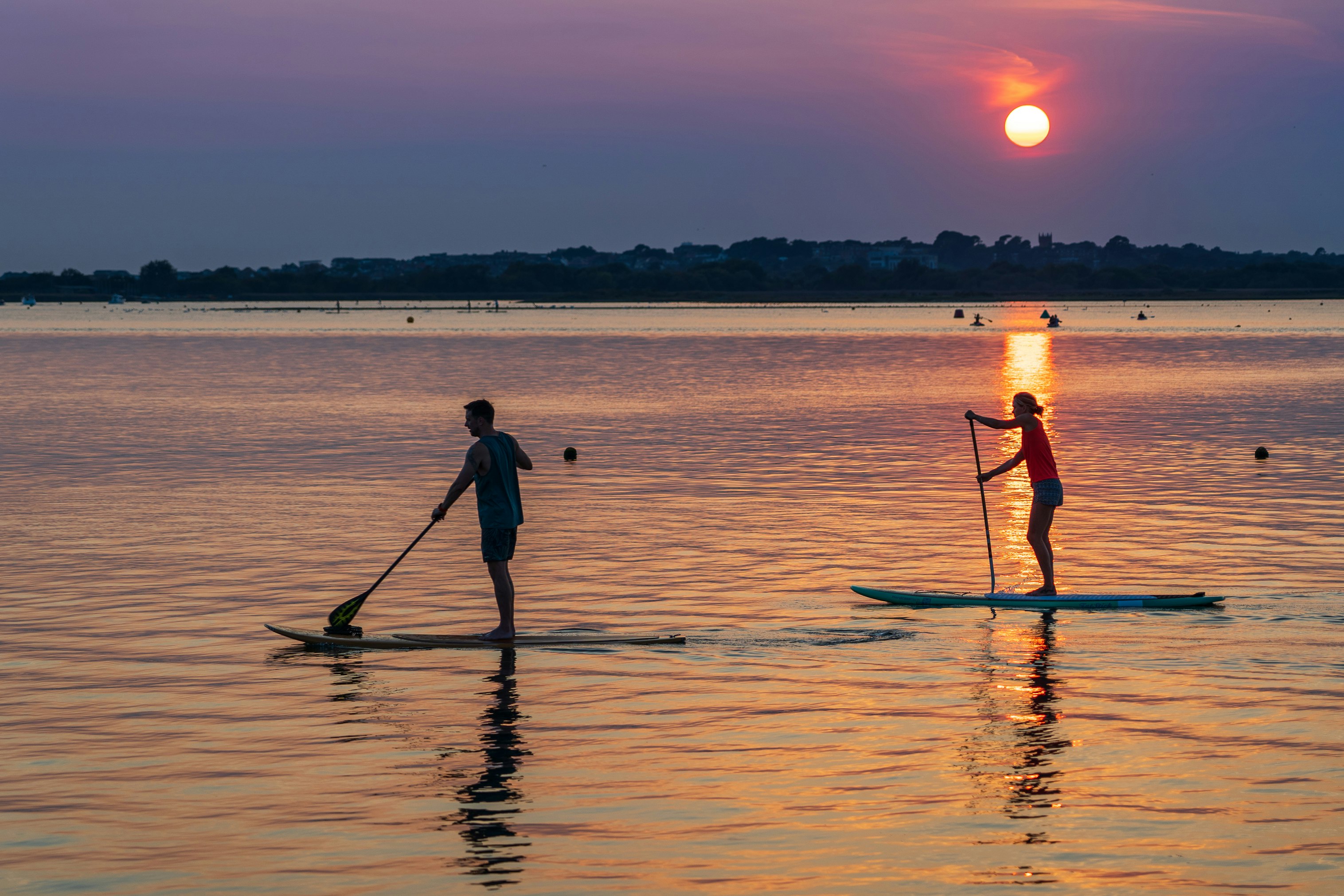 Two people paddle boarding at sunset, during the Summer, silhouetted in the golden light.