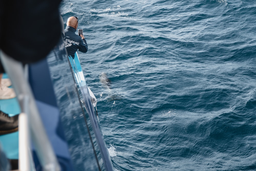 Persona con chaqueta negra y jeans de mezclilla azul de pie en el mar azul durante el día