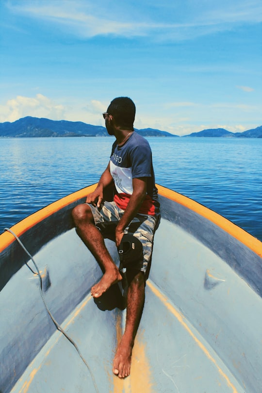 man in blue t-shirt sitting on white and blue boat during daytime in Enarotali Indonesia