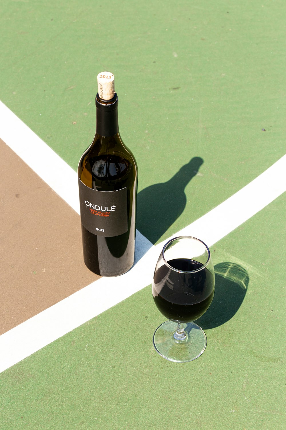 Botella de vidrio negro junto a copa de vino transparente