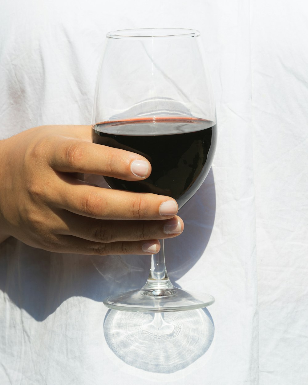 person holding clear wine glass with red wine