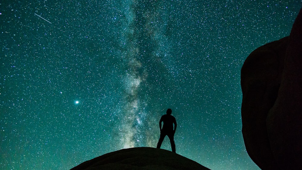 silhouette of man standing on rock under starry night