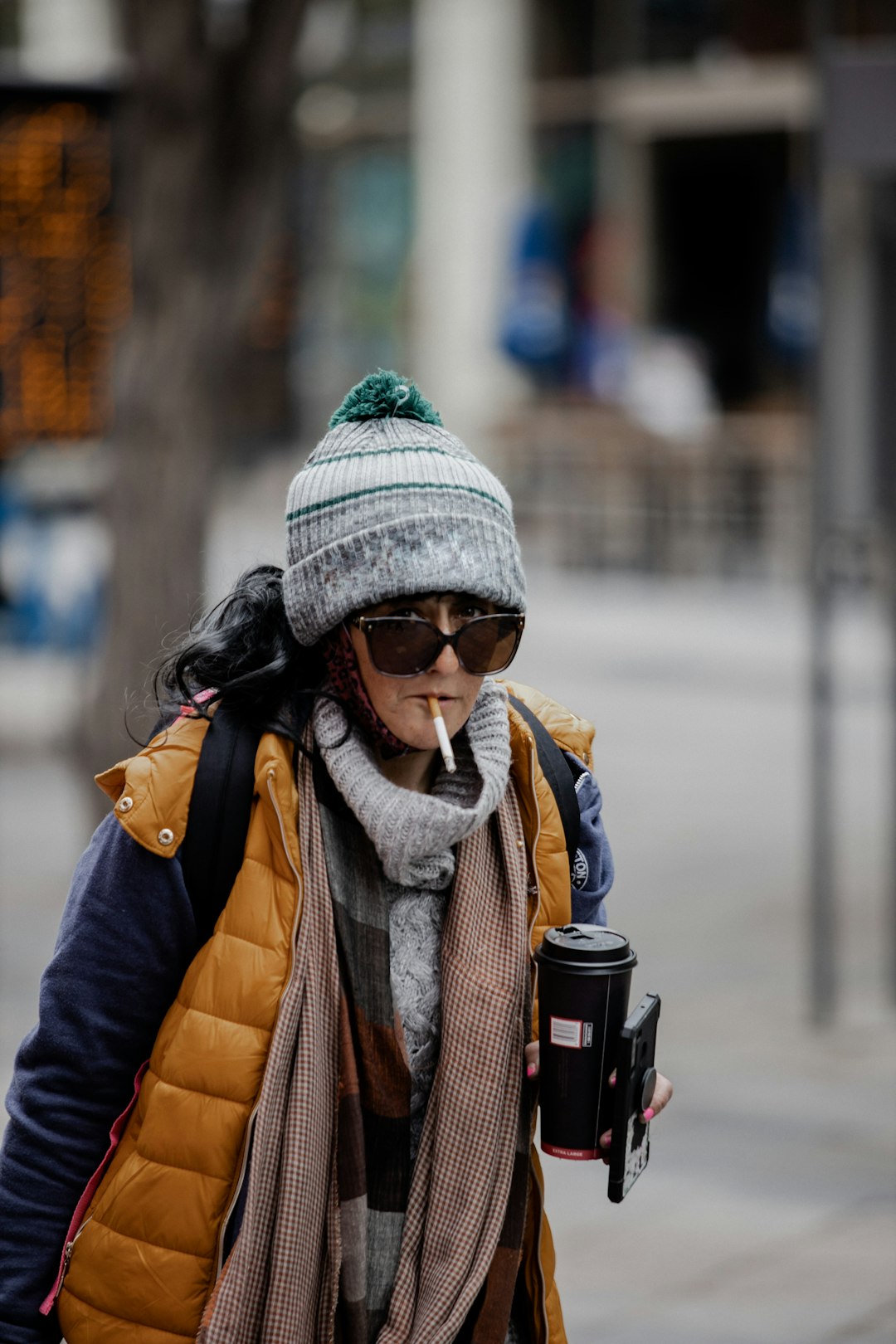 woman in black jacket and white knit cap holding black and red travel mug