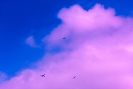 A vibrant sky with a mix of deep blue and pink hues. Several small helicopters or drones are flying in the distance, silhouetted against the colorful clouds.