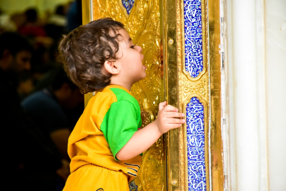 girl in yellow and pink shirt leaning on gold and blue floral wall