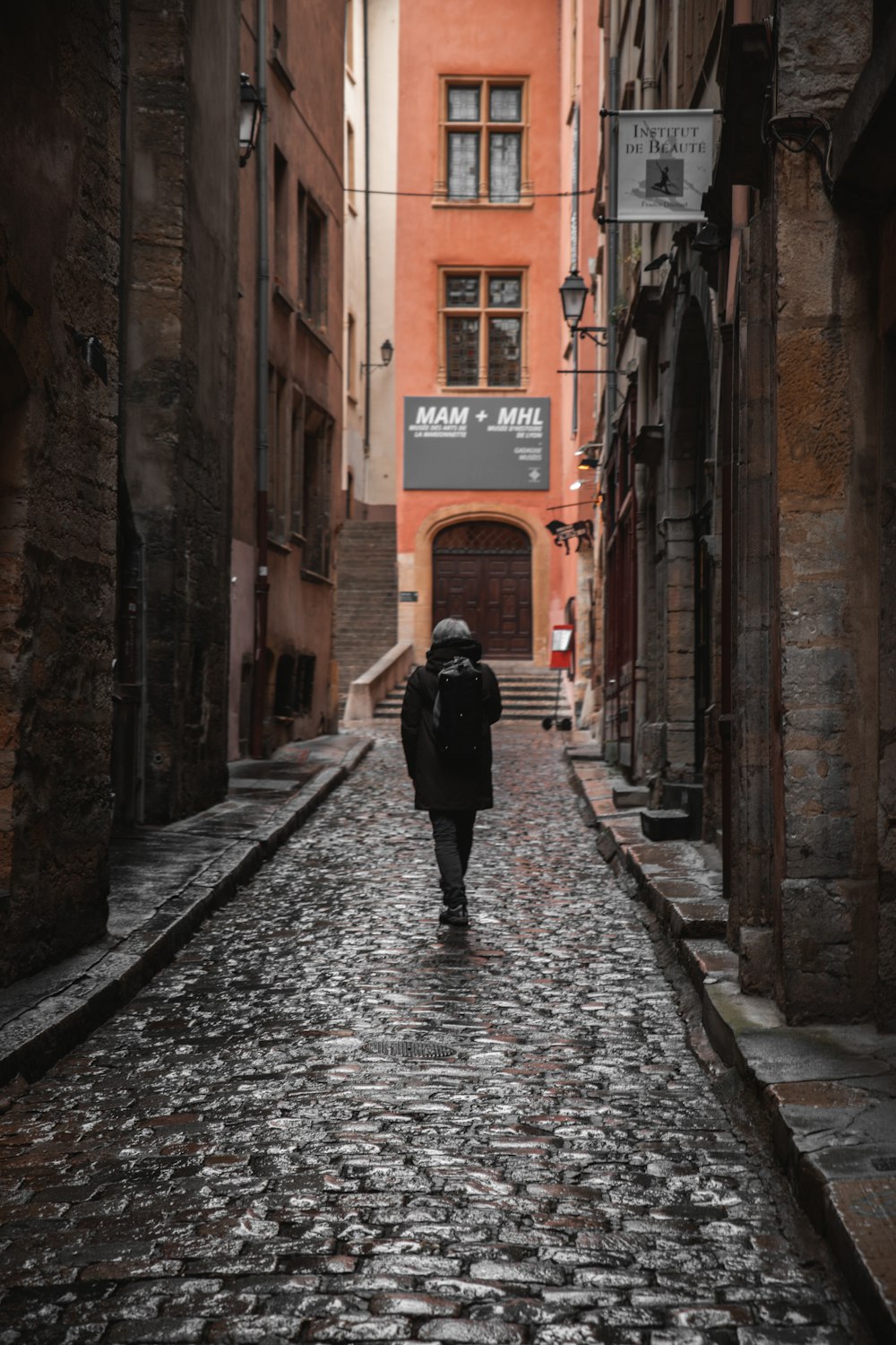 femme en manteau noir marchant dans la rue pendant la journée