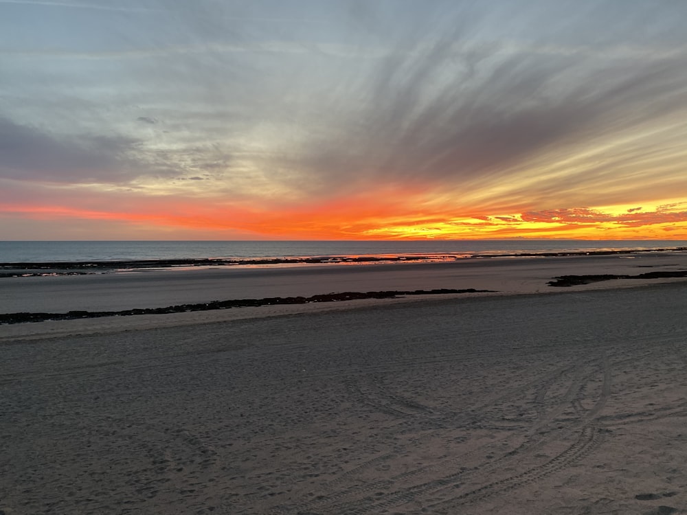 arena gris cerca del cuerpo de agua durante la puesta del sol