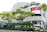 A modern building with a unique, hexagonal-patterned facade featuring green plants integrated into the design. The building has large, prominent advertisements and storefronts including Uniqlo. Several vibrant green trees with yellowish leaves line the street in front of the building. A traffic sign is visible, directing towards Middle Road and Beach Road. Cars are parked or moving by the roadside.